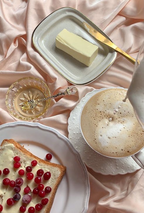 Inviting breakfast scene with buttered toast, cranberries, and a latte on pink fabric.