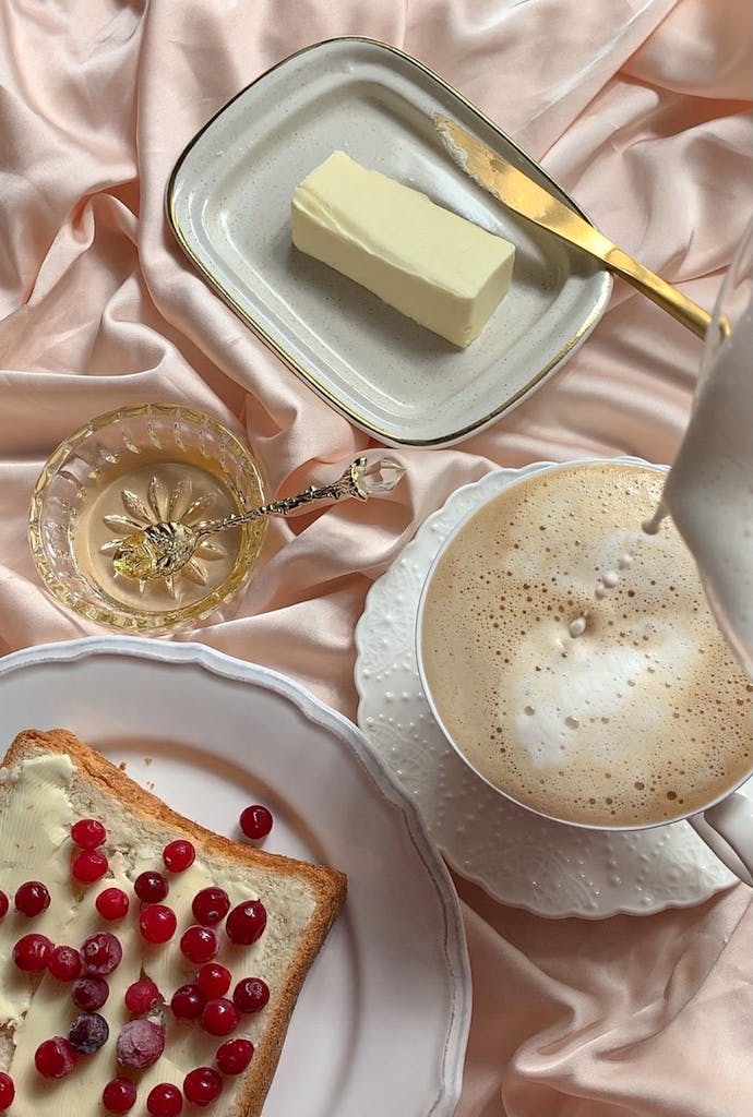 Inviting breakfast scene with buttered toast, cranberries, and a latte on pink fabric.